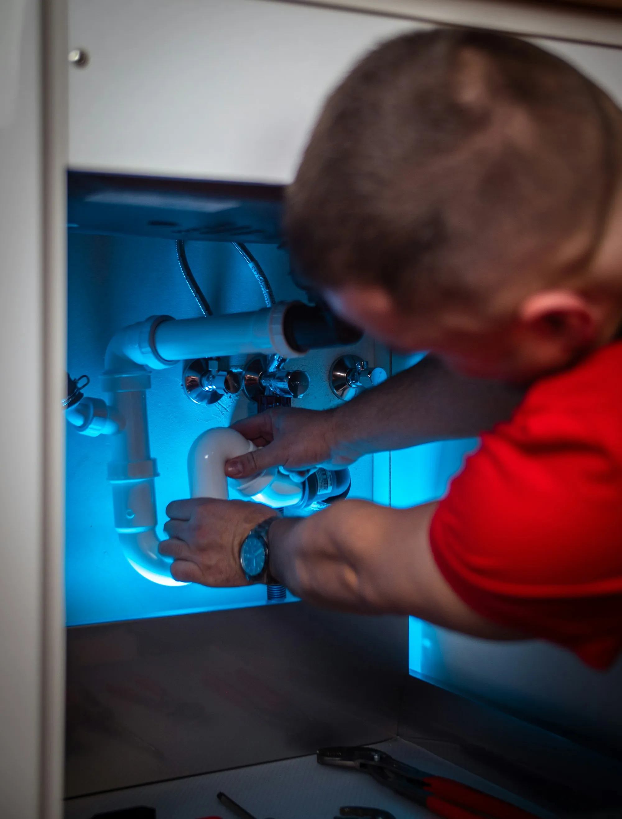 Local Water Specialists, Not a Sales Floor Plumber working on the pipes inside a sink cabinet